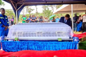 Casket of Evelyn Kujinga at Glen Forest Cemetery during funeral service, surrounded by floral tributes.