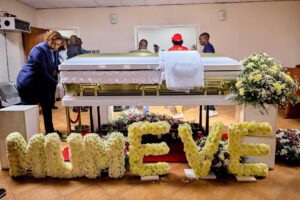 Casket of Evelyn Kujinga at funeral parlour during funeral service, surrounded by floral tributes.